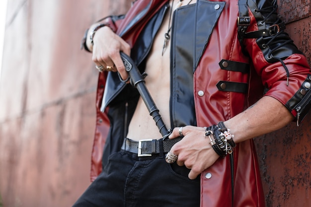 Primo piano di un corpo maschile con un torso nudo in un'elegante giacca di pelle in jeans con arma vintage. ragazzo in abiti alla moda in posa vicino a un muro arrugginito. Stile antiquato.