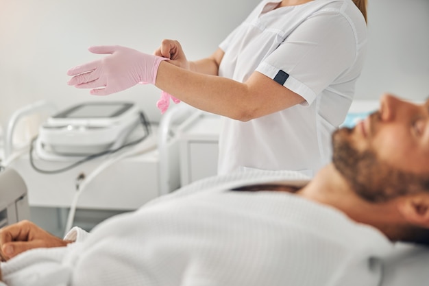 Primo piano di un cosmetologo femminile che indossa guanti rosa mentre si trova accanto al cliente maschio male