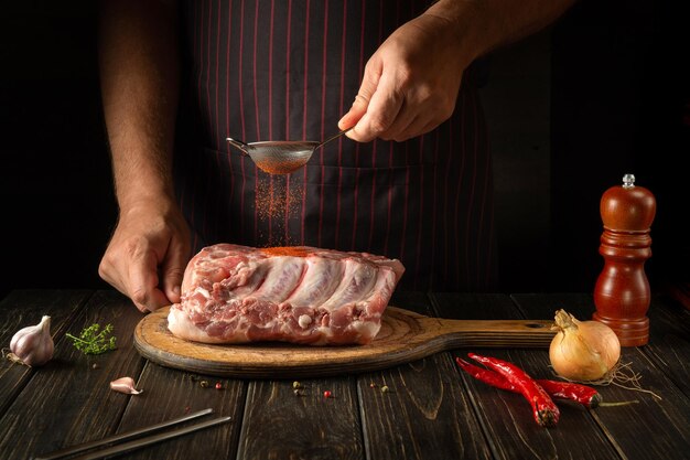 Primo piano di un cuoco che spruzza paprika su costolette di carne fresca Il concetto di cucinare deliziosi cibi di strada o griglia Sfondo scuro con spazio per la pubblicità