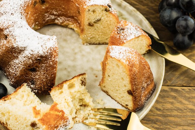 Primo piano di un cupcake affettato con uvetta e zucchero a velo su un piatto e uno sfondo di legno.
