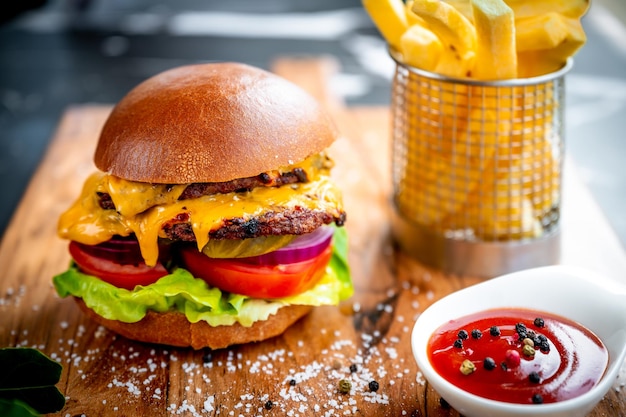 Primo piano di un delizioso doppio cheeseburger con patatine fritte e ketchup su una tavola di legno