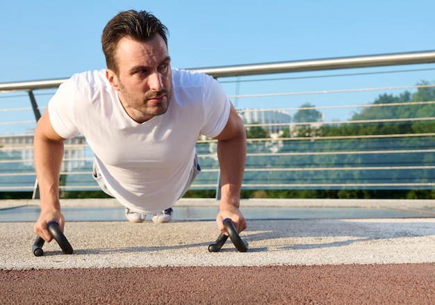 Primo piano di un determinato bell'uomo di mezza età atleta che esercita i muscoli di pompaggio all'aperto mentre esegue flessioni di allenamento sul ponte urbano in una bella giornata estiva