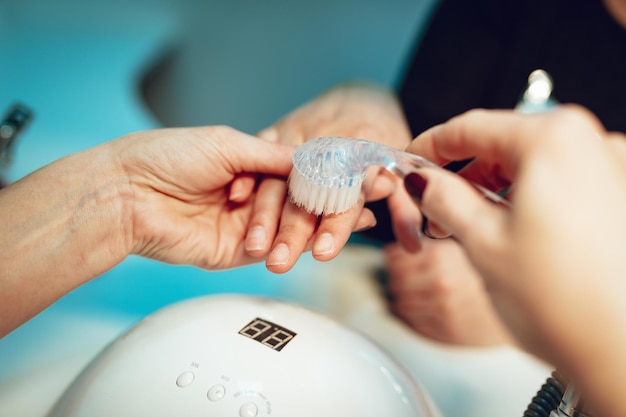 Primo piano di un'estetista che spazzola le unghie dei clienti femminili per il processo di manicure presso il salone di bellezza.