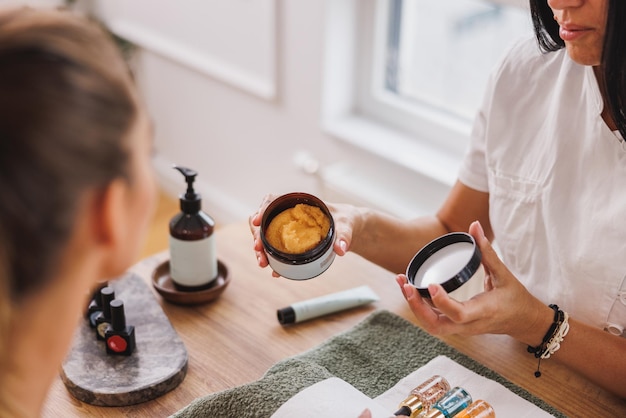 Primo piano di un'estetista irriconoscibile che mostra la crema peeling per lo scrub delle mani al cliente durante il trattamento di manicure.