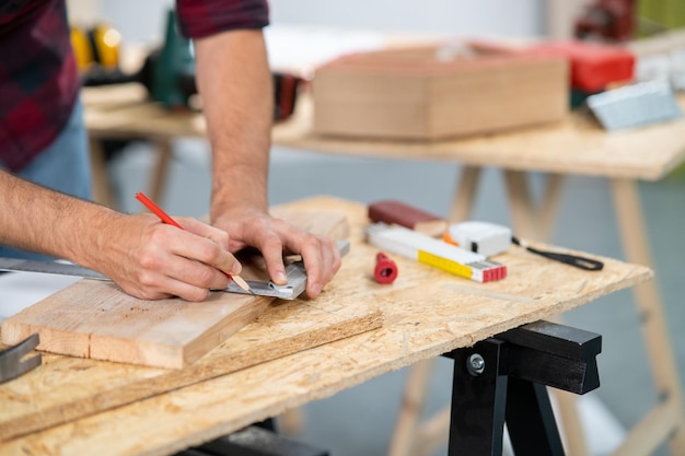 Primo piano di un falegname professionista laborioso che tiene un righello e una matita angolari mentre misura a