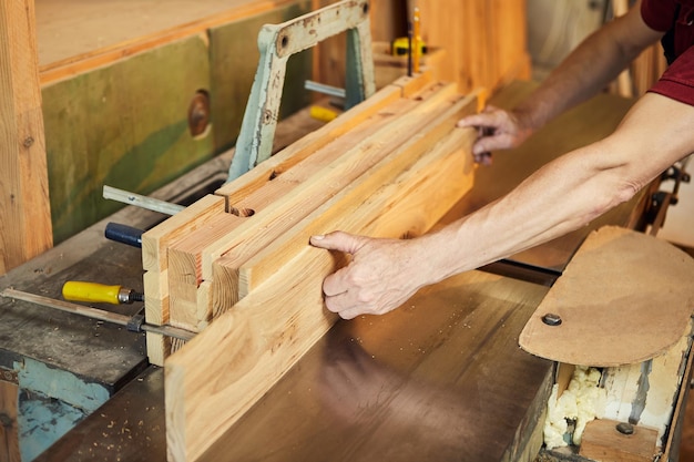 Primo piano di un falegname senior in uniforme lavora su una macchina per la lavorazione del legno presso la produzione di falegnameria