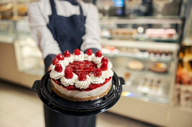 Primo piano di un fornaio che tiene una torta e la mostra a una telecamera mentre si trova al supermercato