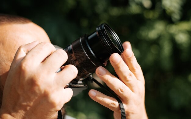 Primo piano di un fotografo che tiene in mano una fotocamera digitale e fotografa qualcosa all'aperto in una giornata di sole. Vista laterale di un uomo che tiene una lente, concetto di hobby. Persona irriconoscibile