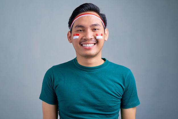 Primo piano di un giovane asiatico sorridente in maglietta casual che guarda la fotocamera isolata su sfondo grigio concetto di celebrazione del giorno dell'indipendenza dell'Indonesia