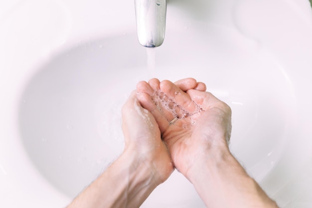 Primo piano di un giovane che si lava le mani con il sapone nel lavandino o