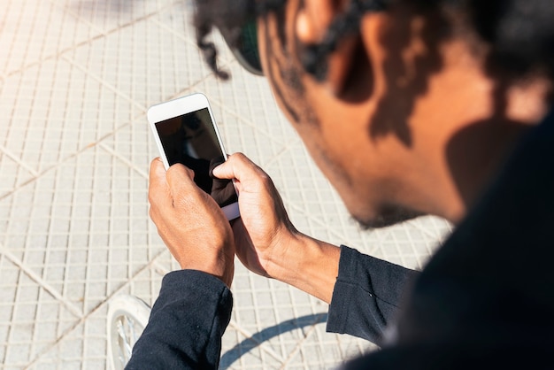 Primo piano di un giovane che utilizza il telefono cellulare e la bicicletta a scatto fisso in strada.