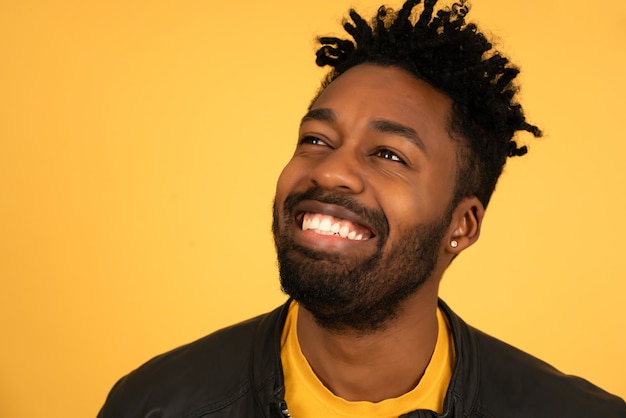 Primo piano di un giovane uomo afro che sorride mentre si trova su sfondo giallo isolato.