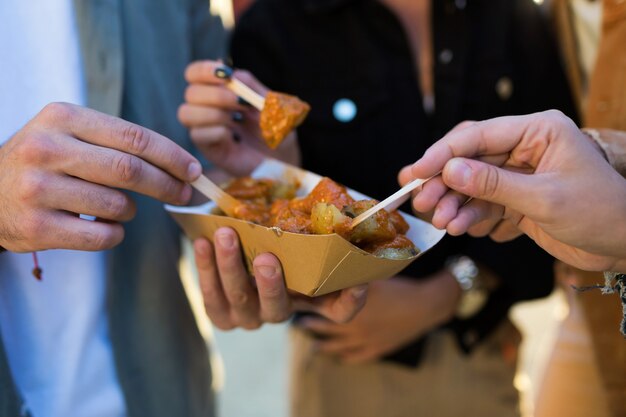 Primo piano di un gruppo di amici che visitano il mercato e mangiano patate per strada.