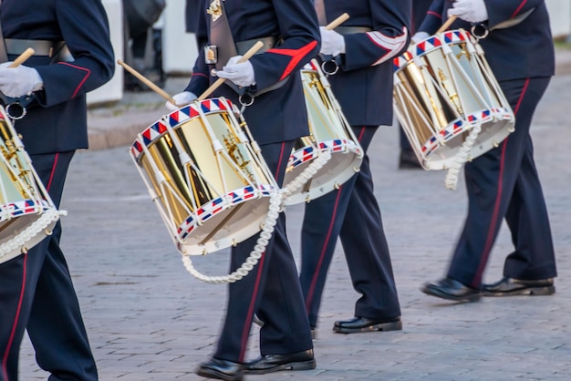 Primo piano di un gruppo di batteristi in uniforme che marciano all'unisono lungo una strada cittadina, suonando la batteria