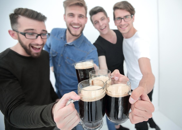 Primo piano di un gruppo di giovani uomini felici che tintinnano bicchieri di birra isolati su bianco