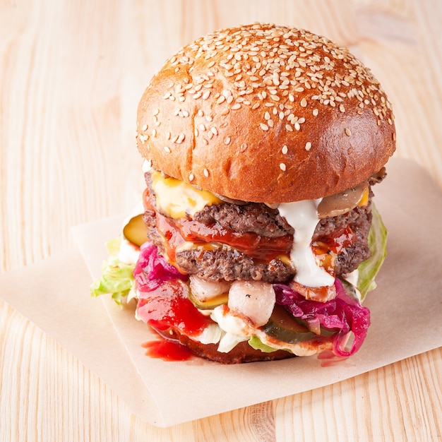 Primo piano di un hamburger di sesamo fresco sul bordo di legno bianco con ketchup e salsa bianca, formaggio, funghi e cipolla rossa. Colpo quadrato