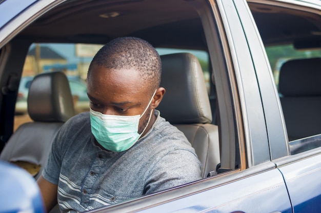 Primo piano di un maschio nero con una maschera medica seduto in macchina - il nuovo concetto normale