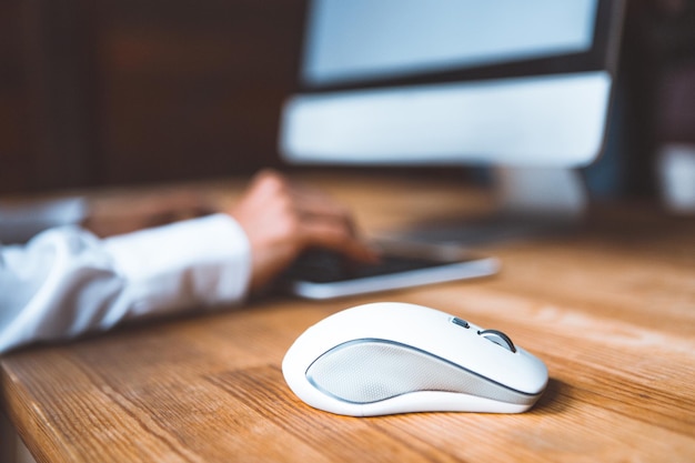 Primo piano di un mouse per computer su un tavolo sullo sfondo di una ragazza che lavora a un vestito da computer...