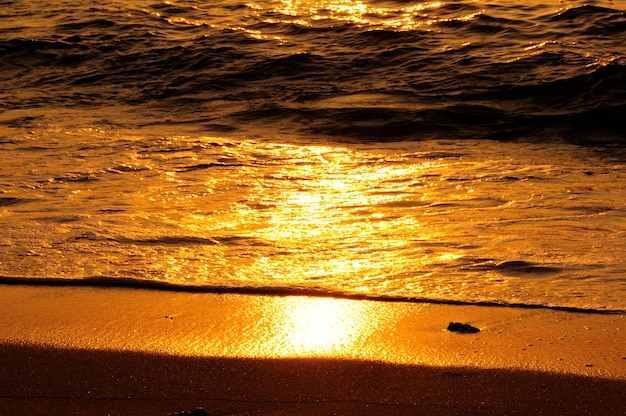 Primo piano di un'onda di colore dorato e sabbia in riva al mare al tramonto.