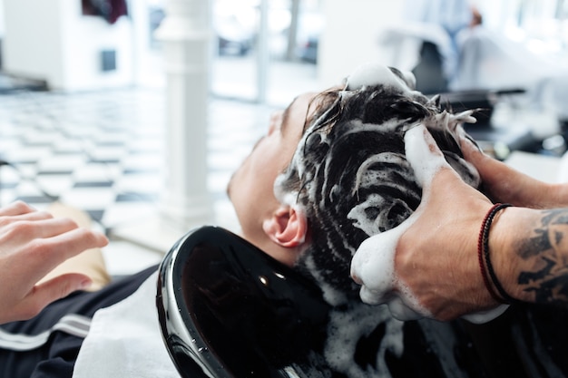 Primo piano di un parrucchiere che lava i capelli del cliente in un barbiere