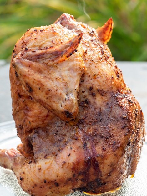 Primo piano di un pollo succoso brillante in spezie cotto alla griglia interamente adagiato su un piatto da portata. grigliata in sottofondo.