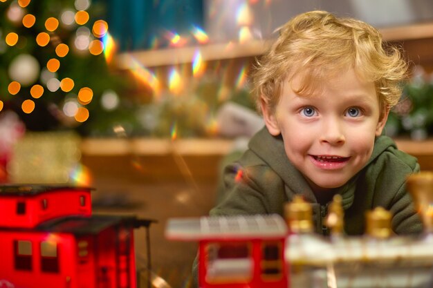 Primo piano di un ragazzo dai capelli ricci che gioca con un trenino magico all'albero di Natale