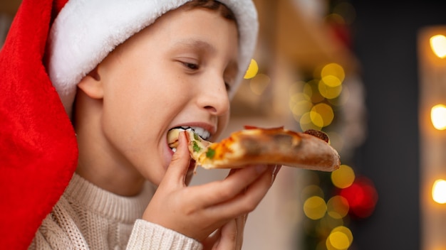 Primo piano di un ragazzo felice con santa cappello mangiare la pizza
