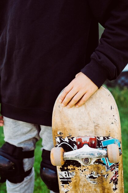 Primo piano di un ragazzo skater con un vecchio skateboard davanti a un murale di graffiti