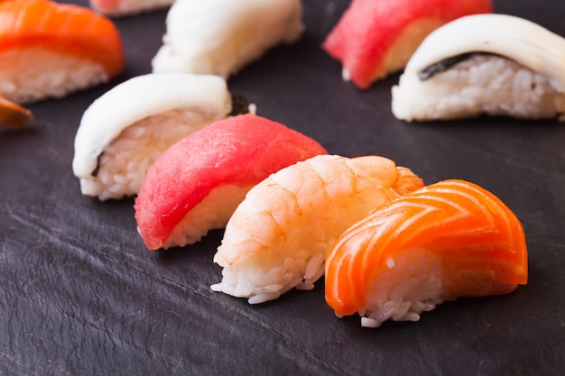 Primo piano di un set di quattro sushi con salmone, tonno, capesante e gamberi su sfondo nero