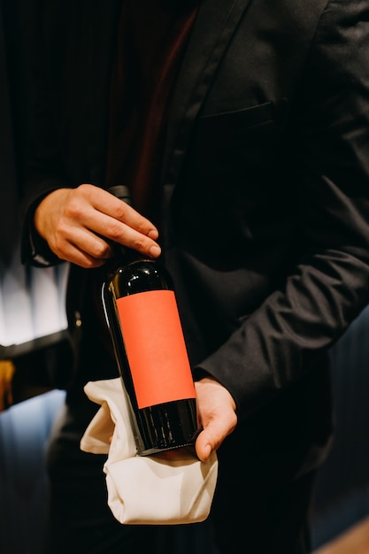 Primo piano di un sommelier che tiene una bottiglia in bianco di vino rosso.