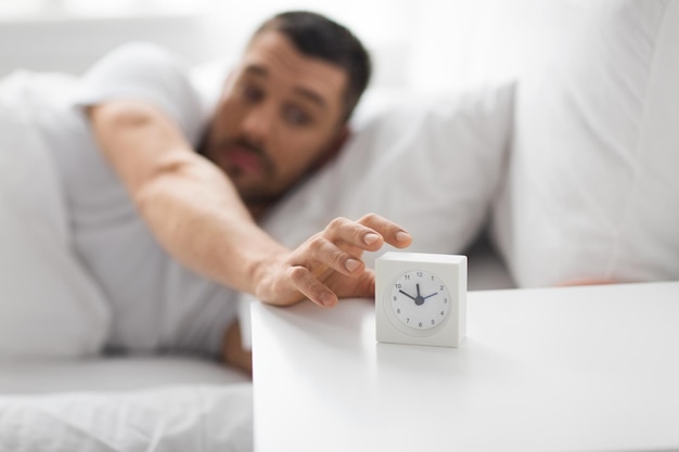 primo piano di un uomo a letto che cerca la sveglia
