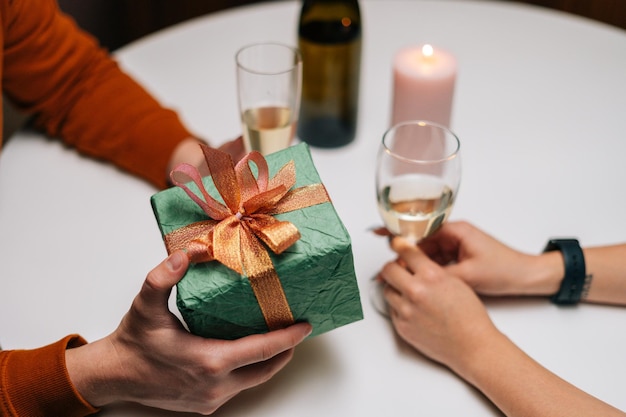 Primo piano di un uomo amorevole irriconoscibile che dà una scatola con un regalo alla donna seduta al tavolo con le candele per il compleanno o il giorno di San Valentino. Moglie felice che riceve un regalo dal marito che si gode una cena romantica