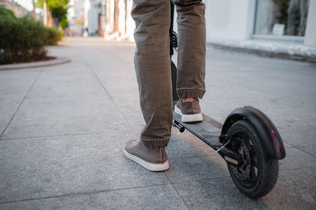 Primo piano di un uomo che guida uno scooter elettrico nero al paesaggio urbano al tramonto