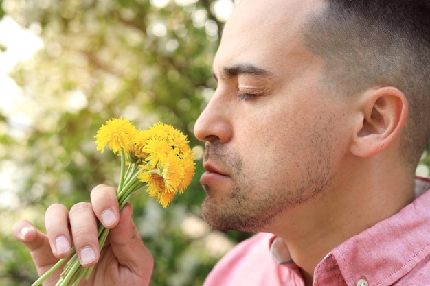 Primo piano di un uomo che sente l'odore dei denti di leone nel parco