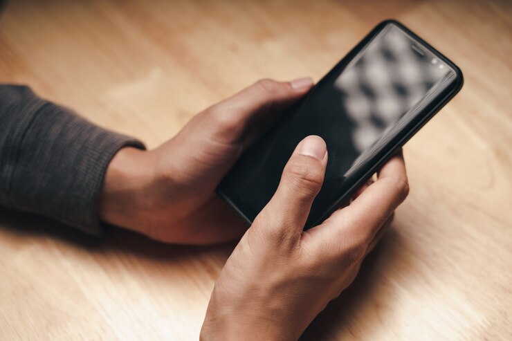 Foto primo piano di un uomo che utilizza uno smartphone sul tavolo di legno, ricerca, navigazione, social media, messaggi, e-mail, marketing digitale su internet, shopping online.