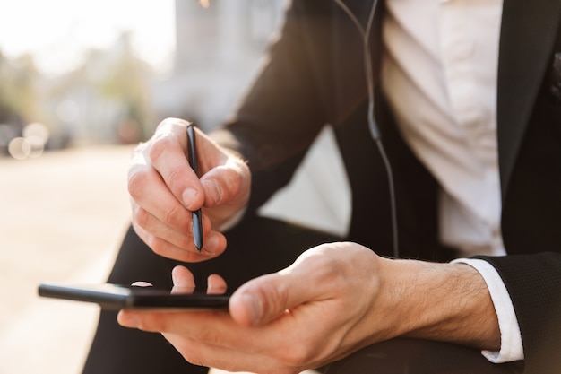 Primo piano di un uomo d'affari che utilizza il telefono cellulare e lo stilo all'aperto