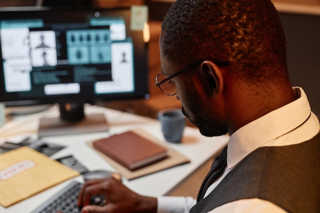 Primo piano di un uomo nero come detective della polizia che utilizza il computer sul posto di lavoro nello spazio della copia dell'ufficio