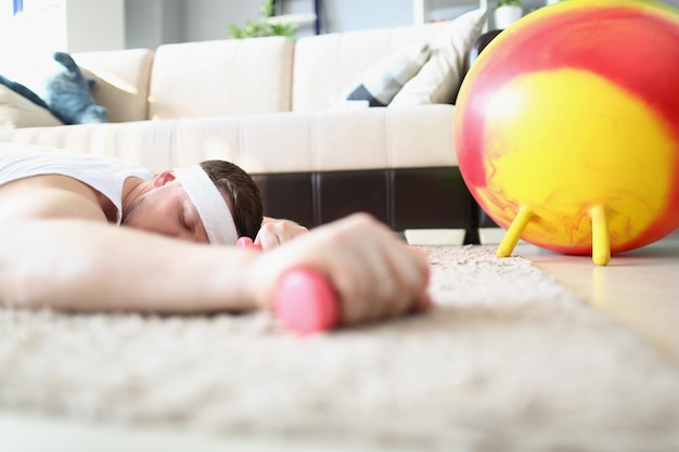 Primo piano di un uomo stanco sdraiato sul pavimento con manubri in mano. Lo sportivo esausto dopo i duri esercizi si è addormentato. Casa, concetto di sport