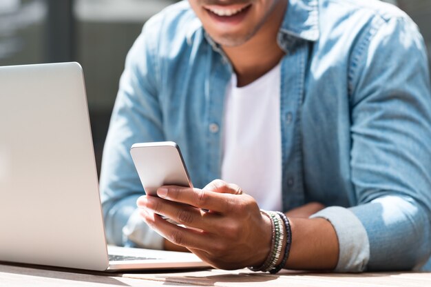 Primo piano di un uomo studente utilizzando smart phone e laptop nella caffetteria