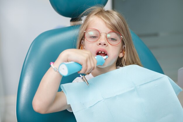 Primo piano di una bambina adorabile che si lava i denti con lo spazzolino elettrico nell'ufficio del dentista