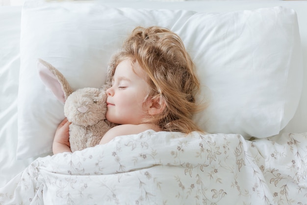 Primo piano di una bambina che dorme e che abbraccia il suo coniglio di peluche. Rilassamento. Sonno sano. Accogliente.