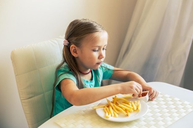 Primo piano di una bambina che mangia patatine fritte in cucina