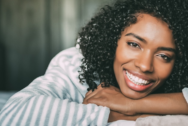 Primo piano di una bella donna nera con i capelli ricci, sorridente e disteso sul letto guardando la telecamera