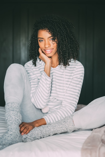 Primo piano di una bella donna nera con i capelli ricci sorridente seduto sul letto guardando la telecamera