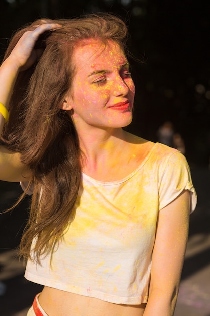 Primo piano di una bella modella bruna ricoperta di polvere Holi, in posa alla luce del sole