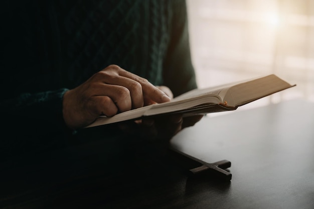 Primo piano di una Bibbia aperta con una croce per la devozione mattutina su un tavolo di legno con luci di finestra