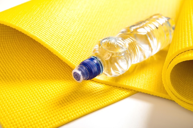 Primo piano di una bottiglia di acqua naturale e di un tappetino fitness giallo