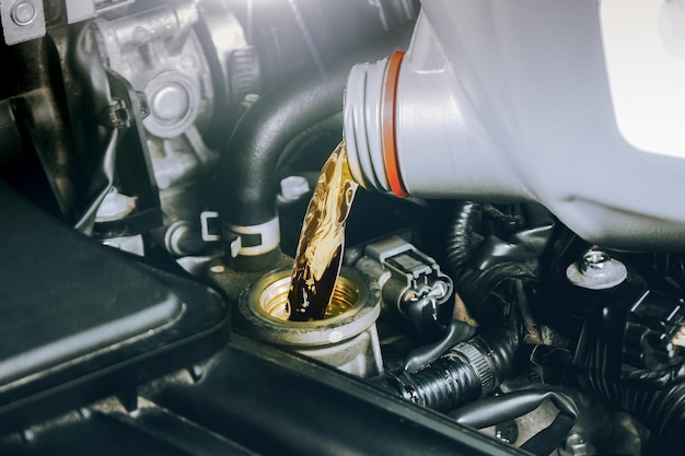 Primo piano di una bottiglia di olio motore che viene versato in un motore a combustione per auto per lubrificare Cambio dell'olio nel motore dell'auto Concetto di servizio di manutenzione automatica