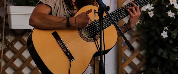 Primo piano di una chitarra spagnola tenuta da una persona davanti a un microfono