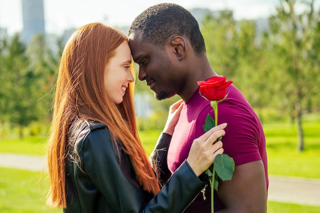 Primo piano di una coppia interrazziale che tiene una rosa bianca nel parco autunnale di primavera